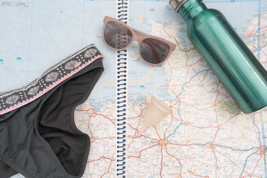 travelling with a menstrual cup - a bunch of travel accessories including a bikini, sunglasses, a map, a water bottle and a Mooncup