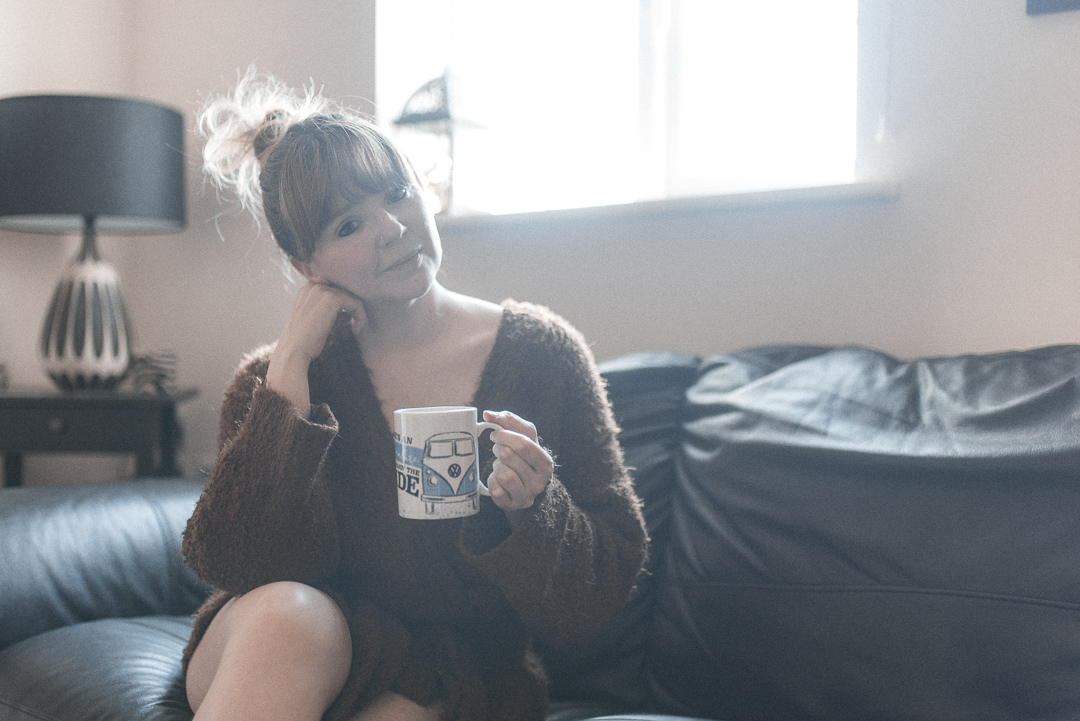 eating disorder recovery in lockdown - Beth Anne sits on the sofa in a furry jumper with a cup of tea